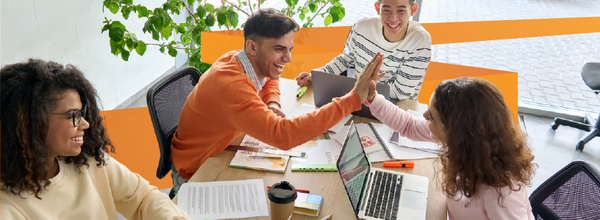 Higher education students high five over laptops in library