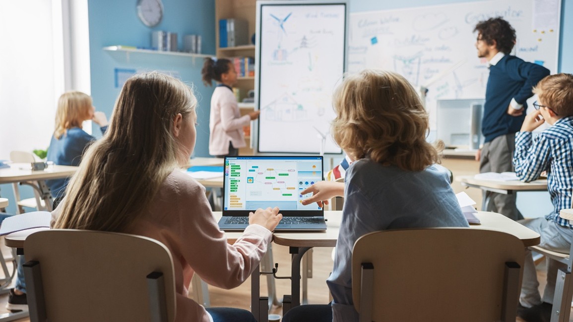 male teacher helping student and students looking on laptop. 