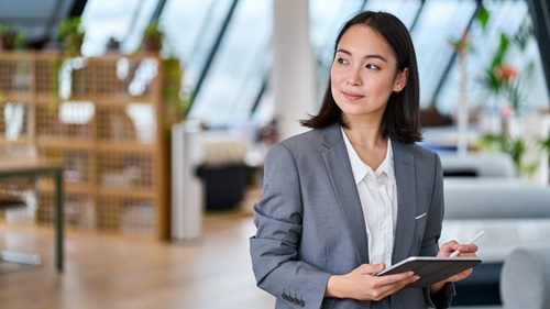 Executive in blazer holding tablet gazing to their right in thoughtful consideration